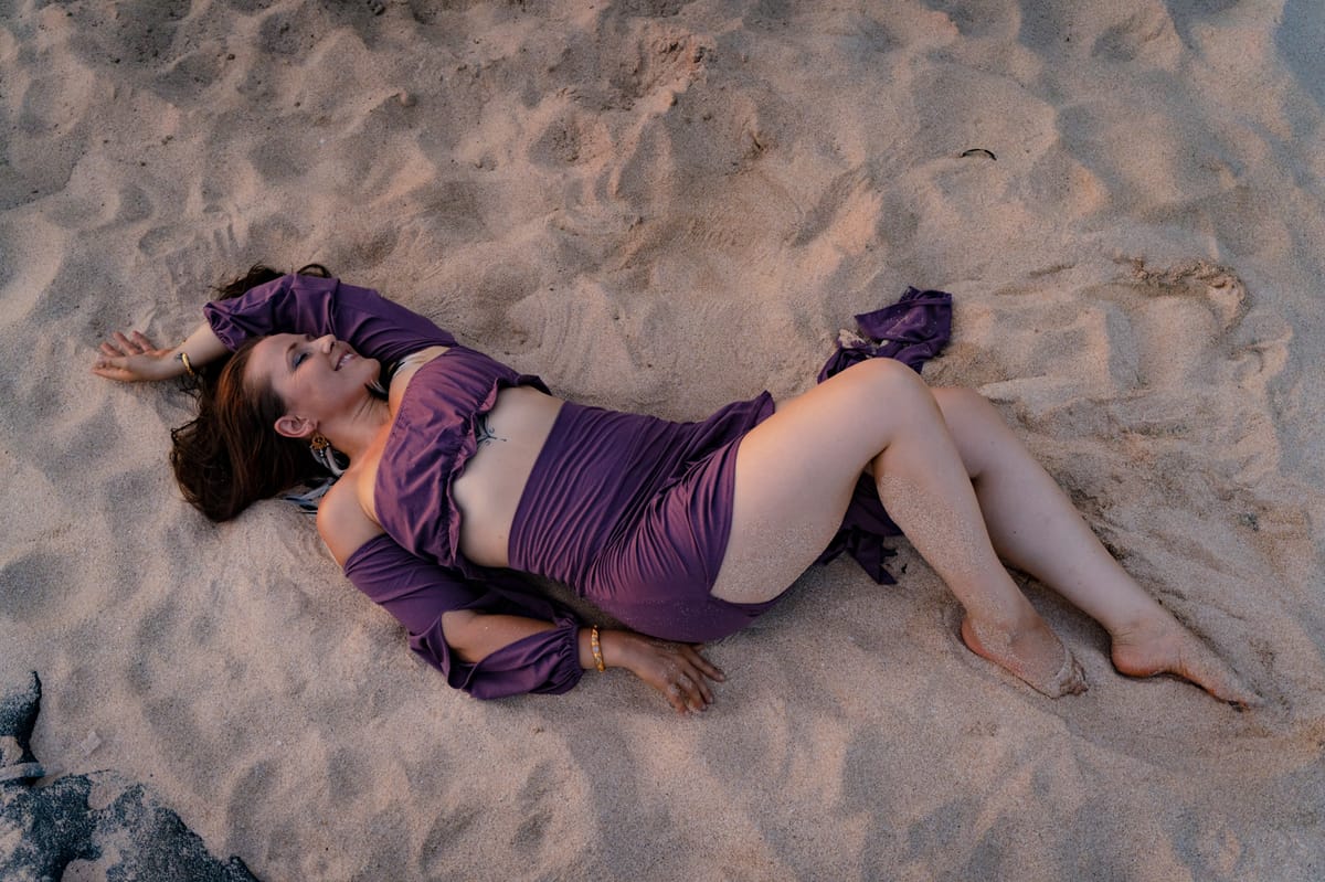 Sara lying in the sand in a purple outfit