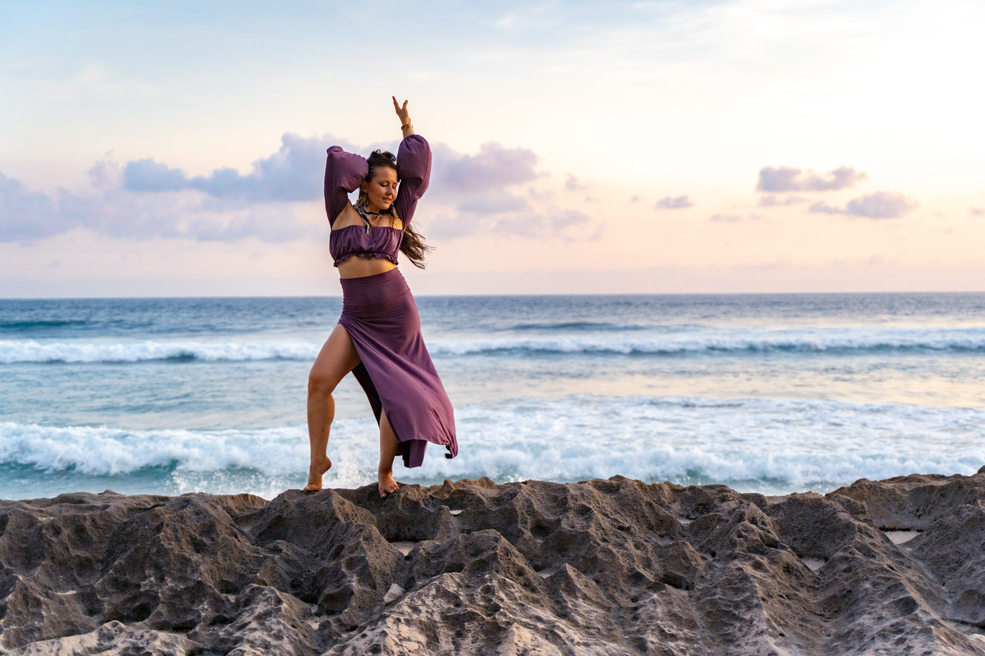 Sara Adolfsen Somatic educator is standing on a cliff with hand in the air, feeling fully safe, free and alive in her body.